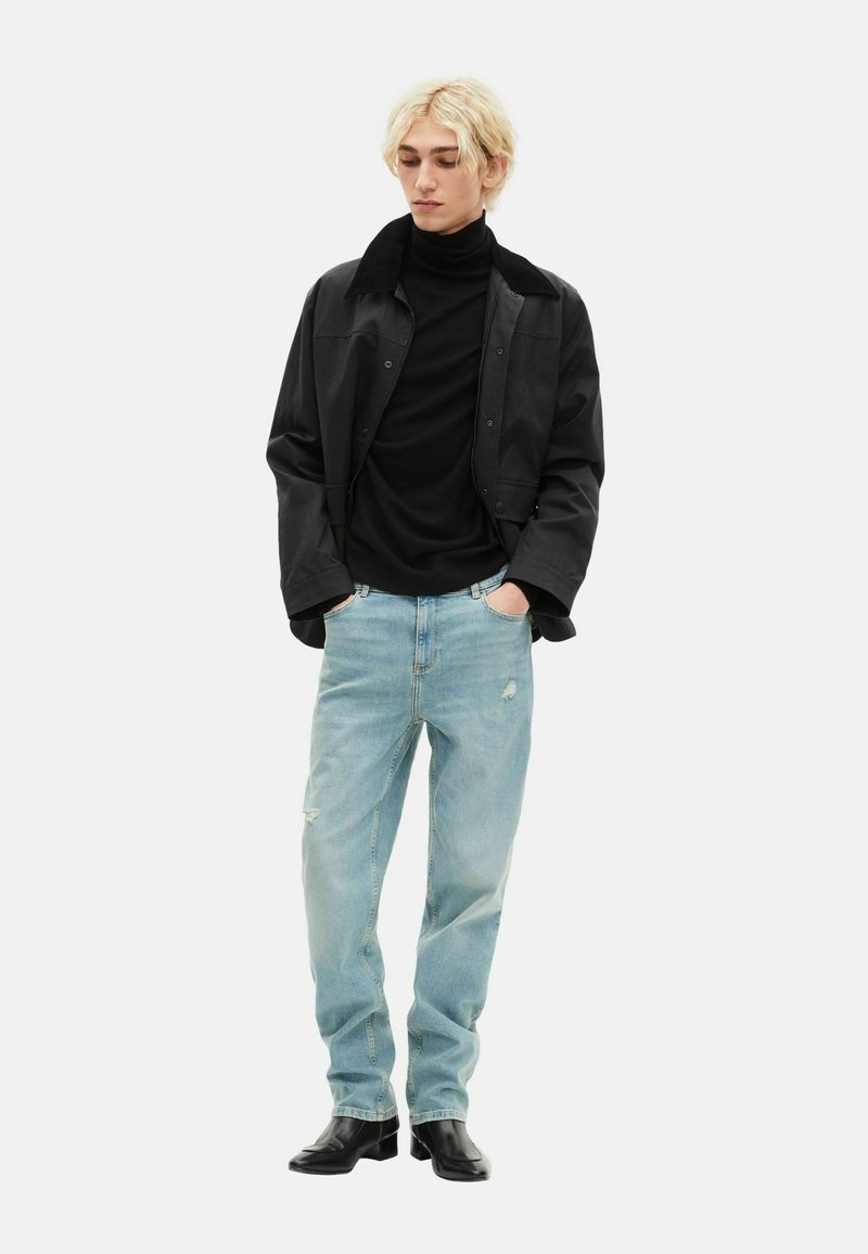 Black collared jacket over a black turtleneck, paired with light blue distressed jeans and black leather ankle boots.