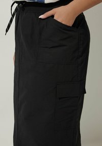 Svart cargokjol i lättviktsmaterial med sidofickor och justerbart midjeband. Designen har sömnadsdetaljer och en slät yta.