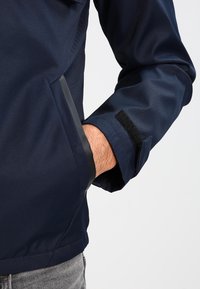 Marinblå jacka med en mjuk textur, elastiska ärmmuddar med kardborrestängning och sidofickor. Vinklad design med en slim fit.