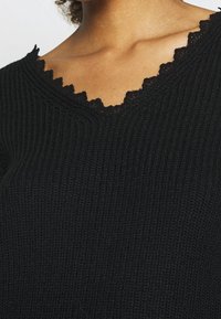 Schwarzes gestricktes Oberteil mit einem V-Ausschnitt und einem gewellten Spitzenrand, das eine gerippte Textur im gesamten Stoff zeigt.