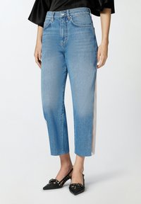 Svijetloplave traperice ravnog kroja s visokim strukom i bijelim bočnim prugama. Tkanina ima blago izblijedjeli završetak.