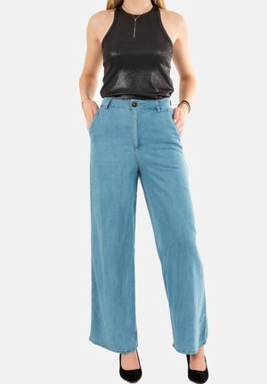 Jean large bleu clair en denim, avec une taille haute, des poches avant et une fermeture à bouton. Associé à un top sans manches noir.