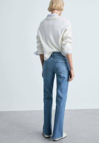 Jeans de mezclilla azul claro con pierna recta, bolsillos traseros y cintura alta, combinados con un suéter blanco de canalé y zapatillas crema.