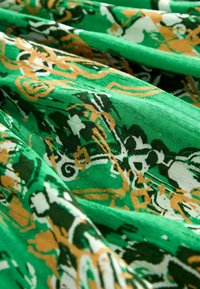 Zielony materiał złożony z misternych wzorów w ciemnozielone, białe i złote spirale. Teksturowana powierzchnia, lekki i zwiewny wygląd.