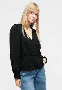 Musta pitkähihainen kietaisupusero, jossa on teksturoitu kangas, pitsireunus pääntiellä ja nyöritys vyötäröllä. Yhdistetty vaaleansinisiin farkkuihin.