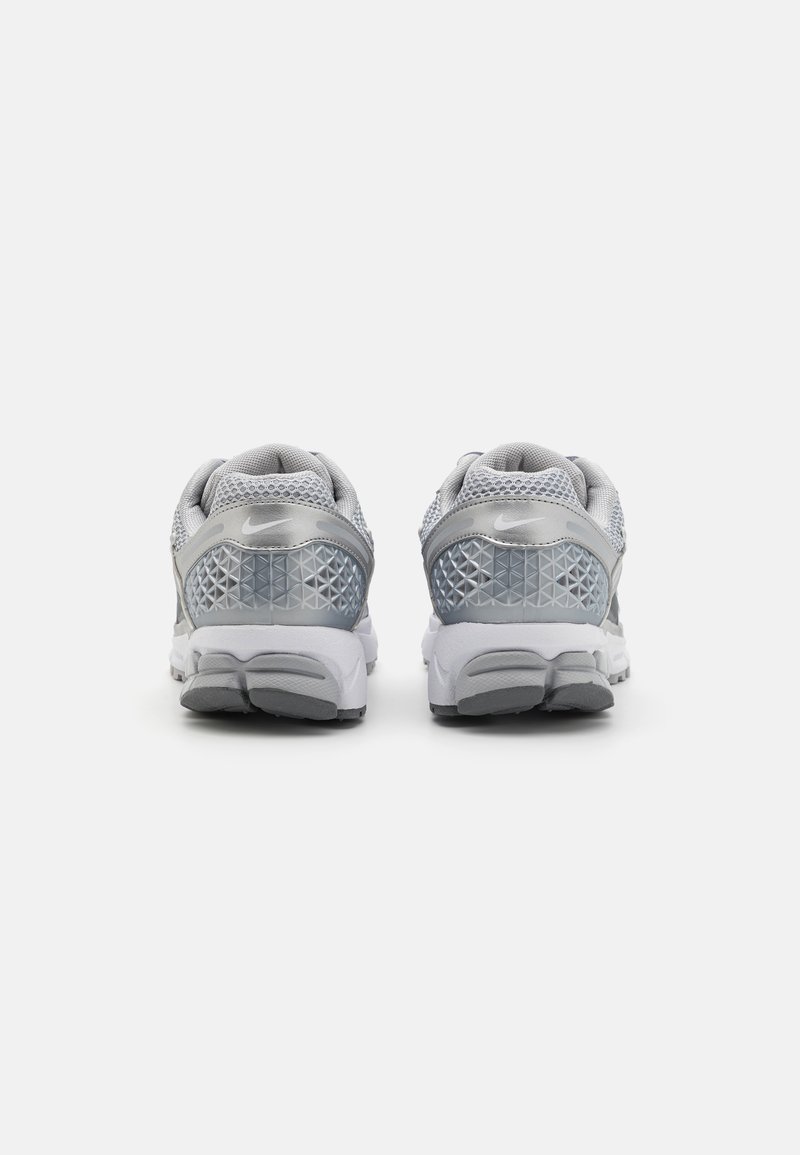 Zapatillas deportivas grises con parte superior de malla, acentos de patrón geométrico, suelas acolchadas y detalles reflectantes en el talón.