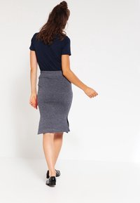 Marinblå t-shirt med korta ärmar, kompletterad med en grå, figurnära kjol med lätt utsvängt fåll och sidöppning, bärs med svarta skor.