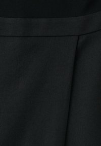 Gros plan sur un tissu noir avec une texture en tissage diagonal et un détail de couture pliée.