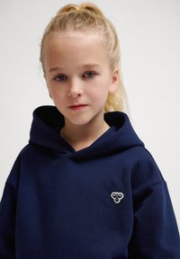 Mörkblå huvtröja i mjukt tyg, med en liten broderad logotyp på bröstet. Texturerad, avspänd passform.