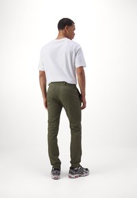 Olive green fitted pants with a smooth texture, back pocket detail, paired with a plain white t-shirt and gray athletic shoes.