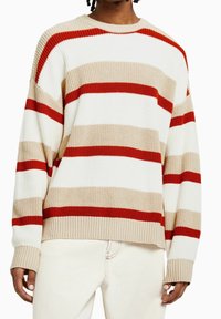 Randig stickad tröja med röda, beige och vita horisontella ränder, ribbat mönster och rund halsdesign.