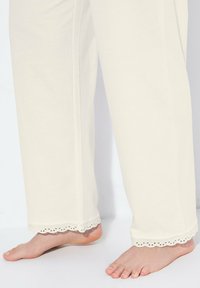 Pantalones de pijama color crema, hechos de una tela suave, con un acento de encaje con forma de ondas en el dobladillo y un ajuste relajado.
