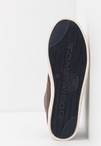Brązowe sneakersy z teksturowaną powierzchnią, gumową podeszwą z falistym wzorem oraz logo "TOM TAILOR". Biała krawędź wokół podeszwy.
