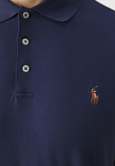 Mornarskopolna polo majica od pamuka, sa tri dugmeta na prednjem dijelu. Istaknut izvezeni logo konjanika u kontrastnim bojama.
