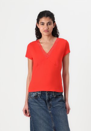 T-shirt rosso con scollatura a V e rifiniture in pizzo, maniche corte, design aderente e texture morbida, abbinato a una gonna di jeans.