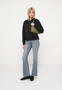 Čierna mikina s kapucňou a šnúrkami, svetlomodré zvonové džínsy, čierne topánky a zelená taška s dekoratívnymi akcentami. Jednoduchý, moderný outfit.