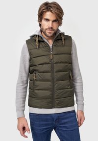 Olivenfarvet polstret vest med lynlåslukning, der har sidelommer og hætte. Den indre lag er grå, med et tekstureret, ribbet ærmedesign.