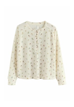 Haut crème à manches longues avec texture côtelée, imprimé floral rose et vert, encolure arrondie, patte de boutonnage, et coupe décontractée.