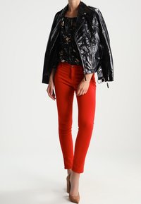 Veste de motard en cuir noir, blouse florale, jean skinny rouge et chaussures beiges à talons hauts. Accent sur les couleurs vives et le contraste des textures.