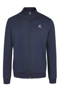 Chaqueta navy con cremallera, fabricada en un tejido suave, que presenta un cuello alto, dos bolsillos frontales y un pequeño logo bordado en el lado izquierdo del pecho.