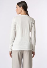 Maglietta bianca a maniche lunghe realizzata in tessuto leggero, con un design semplice e un collo rotondo, abbinata a pantaloni di colore chiaro.