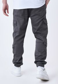 Pantalones cargo grises con puños elásticos, que cuentan con múltiples bolsillos laterales y una textura suave. Llevados con zapatillas blancas.