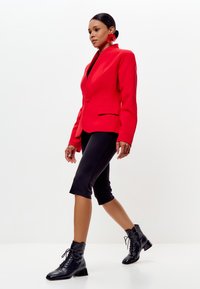 Rode gestructureerde blazer met een sjaalkraag, zwarte cropped leggings en zwarte veterschoentjes tot de enkel. Gladde stof met een getailleerde pasvorm.