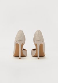 Pump con tacco alto glitter beige, con punta affusolata e tacco stiletto sottile. L'interno presenta un materiale liscio di colore contrastante marrone chiaro.