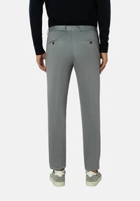 Grijze op maat gemaakte broek van een gestructureerde stof, met twee achterzakken met knoopsluiting en een aansluitende tailleband. Gecombineerd met casual sneakers.