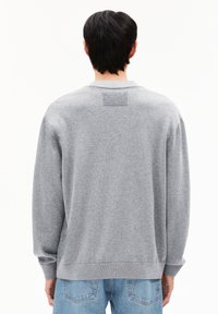 Sweatshirt gris surdimensionné en tissu doux. Il présente un col rond, des poignets côtelés et une pièce rectangulaire au dos.