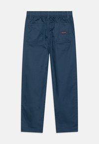 Navy blauwe broek met elastische tailleband, twee achterzakken en een klein logo-patch. Gladde textuur en recht-uitlopend ontwerp.