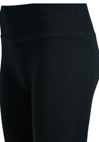 Zwarte leggings met hoge taille en geribbelde textuur langs de zijkanten, gemaakt van rekbare stof. Voorzien van een gladde tailleband en een aansluitende pasvorm.