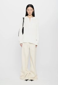 Weiße Bluse mit langen Ärmeln und Kragen, kombiniert mit cremefarbenen weiten Hosen, getragen mit einer schwarzen Schultertasche. Sanfte Texturen und lockere Passform.