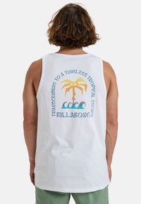 Camiseta sin mangas blanca con un gráfico colorido de una palmera y olas, con texto que dice "Transcendiendo a una escapada tropical atemporal" en la parte de atrás.