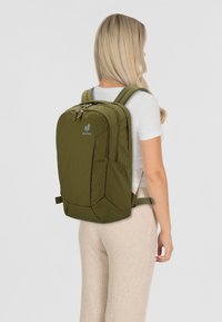 Zaino verde oliva dalla forma rettangolare, realizzato in tessuto resistente, dotato di spallacci imbottiti e di un compartimento principale con zip.