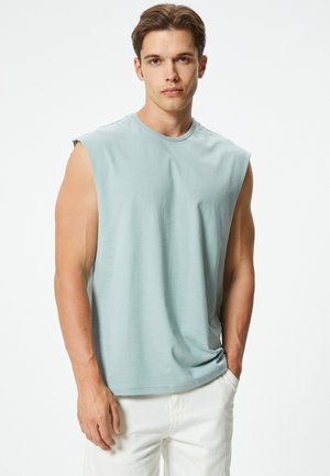 Ärmelloses hellblaues Baumwoll-T-Shirt mit Rundhalsausschnitt und lockerer Passform, kombiniert mit weißen Hosen, die eine glatte Textur und ein einfaches Design aufweisen.