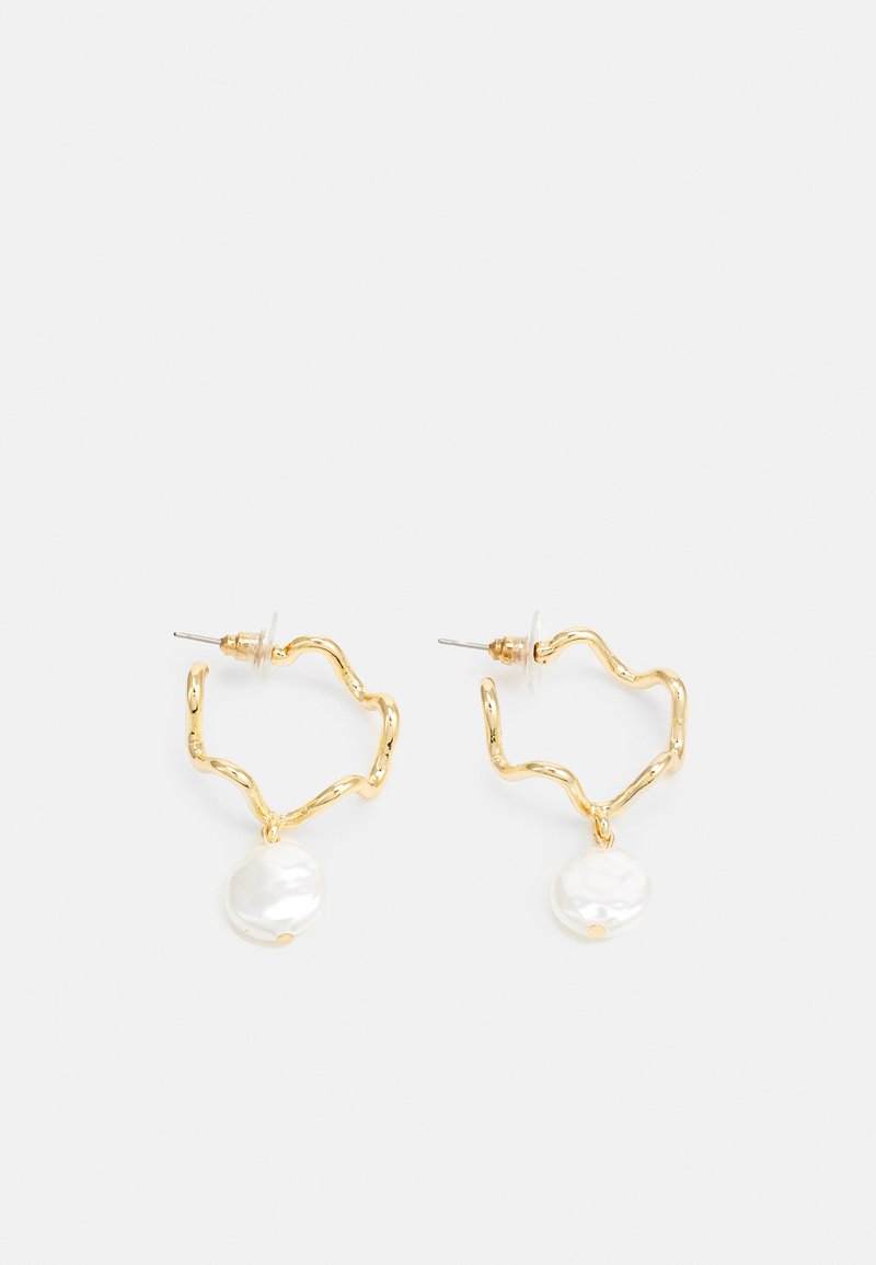 Guldfärgade hoopörhängen med en vågig design, prydda med en vit pärlindroppe. Texturen är slät och hoopörhängena är lätta.