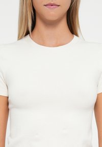 Tricou alb ajustat din țesătură ribbed, cu mâneci scurte și guler rotund. Textura este netedă și ușoară.
