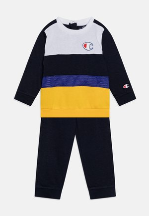 Felpa a maniche lunghe blu navy e bianca con sezioni a righe gialle e viola, caratterizzata da un logo. Pantaloni della tuta neri con polsini. Miscela di cotone.