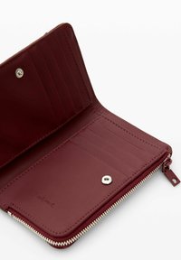 Cartera de cuero burdeos abierta que muestra múltiples ranuras para tarjetas, un bolsillo con botón a presión y una cremallera a lo largo del borde.