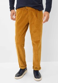 Corduroy broeken in mosterdgeel met verticale ribbels, met een riemlus, knoopsluiting en opgerolde manchetten. Gepaard met marineblauwe sneakers.