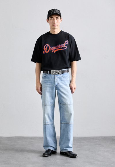 Melna T-kreklu ar sarkano "Dsquared²" logotipu, gaiši zilu vaļīgu džinsu ar aplikācijām, sudrabotu jostu ar "KISS" uzrakstu, melnu cepuri ar studiem.