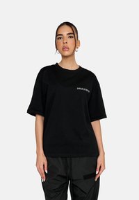 Sort oversized T-shirt lavet af bomuld, med korteærmer, rund hals og et diskret "MULTIPLY" logo i grå på venstre bryst.