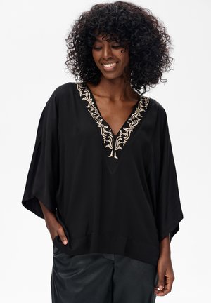 Czarna tunika z szerokim dekoltem w kształcie litery V, zdobiona skomplikowaną beżową haftą. Luźny krój z szerokimi rękawami, wykonana z miękkiego materiału.
