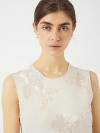 Blouse sans manches en tissu rose clair, ornée de motifs floraux en relief. Le design met en avant des détails élaborés et une texture lisse.