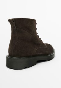 Stivale alla caviglia in suede marrone con una finitura testurizzata, allacciatura frontale e una robusta suola in gomma nera con un motivo a tasselli.