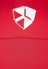 Rødt tekstureret stof har et broderet hvidt logo, der ligner en geometrisk form øverst.