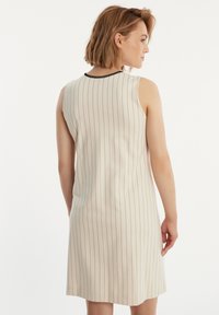 Mouwloze beige jurk met verticale zwarte strepen, voorzien van een zwart accent bij de halslijn. Gladde stof met een aansluitende silhouet.