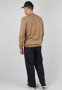 Pull en tricot marron à manches longues, coupe décontractée, avec un ourlet côtelé ; associé à un pantalon sombre et des baskets confortables. Fond uni.