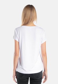 Biała bawełniana koszulka z krótkim rękawem, okrągłym dekoltem i gładką teksturą. Ma luźny krój i lekko zaokrąglony dół z tyłu.